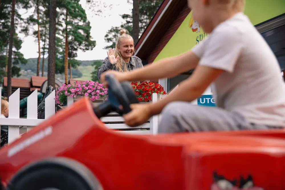 Mor står å vinker til barnet sitt som kjører el-bil